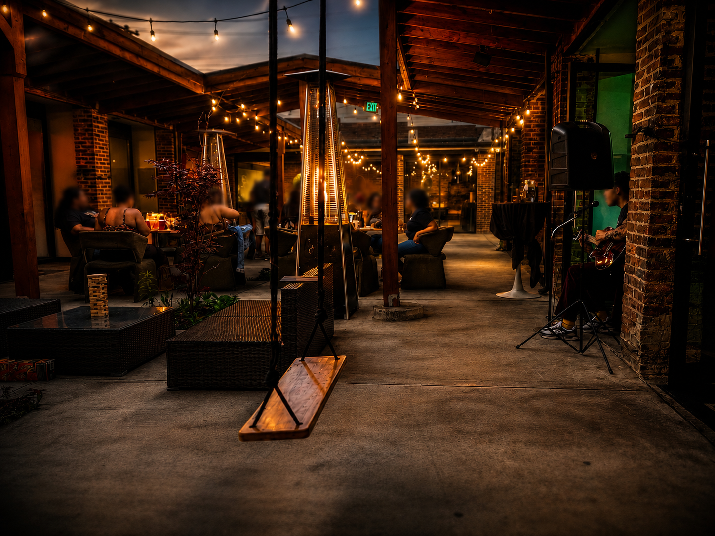 Brick Bistro courtyard at dusk with string lights, fire heaters, live acoustic music, and guests dining